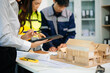 © laddawan - Engineering team planning construction project with blueprint and house model. Collaboration, design, and real estate development concept in modern workspace.