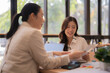 © Tj - Two professional Asian women discussing documents and business strategy during a collaborative meeting in a modern office, focusing on teamwork and partnership