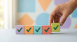 © Rohan Katwe - hand places wooden block cube with checkmark, completing row of similar colorful blocks. task completion, goal achievement, or project success. sense of accomplishment and progress. geometric shapes