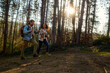 © DusanJelicic - Young adult couple enjoying an outdoor hiking adventure in a sunny forest during autumn, using trekking poles while walking uphill, representing healthy lifestyle and active leisure
