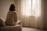 Person sits on a sofa and looks out the window at a view with soft light in a room during daytime