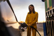 © Home-stock - Woman driver standing at gas station holding fuel nozzle and filling her car with gas or petrol with sunset on background