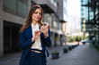© SISMIZ - Businesswoman using smartphone walking on city sidewalk