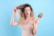 © New Africa - Unhappy woman trying to brush her tangled hair on light blue background