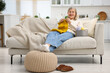 © New Africa - Senior woman knitting with needles on sofa at home