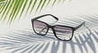 © Luthfi - Stylish sunglasses resting on a white surface with palm leaf shadows