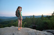 © bilanol - Hiker woman standing on mountain footpath enjoying evening nature during her travel on wilderness trail. Lonely female traveler traversing high hilltop route. Healthy lifestyle concept