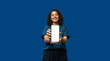 © Milan - Smiling young woman showing blank smartphone screen on blue background. Happy female holding mobile phone for app mockup or digital advertisement. Copy space for text