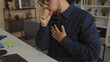 © Krakenimages.com - Man coughing into fist with hand on chest at desk in building office wearing navy shirt and glasses; discomfort recovery.