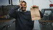 © Krakenimages.com - Hispanic man with beard holding a paper bag and making an ok gesture with his hand over one eye in a restaurant kitchen building; friendly service.