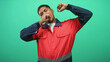 © Krakenimages.com - Hispanic man in red work uniform yawns with hand to mouth and raises arm on a green studio backdrop; tired duty.