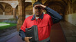 © Krakenimages.com - Man worker holding toolbox and smiling, wearing red uniform with beard visible while standing in an arched building corridor; service readiness confidence.