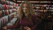 © Krakenimages.com - Woman smiling while browsing colorful books and gesturing with one hand among crowded shelves in a bookstore; joyful curiosity.