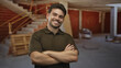 © Krakenimages.com - Man smiling with arms crossed wearing brown polo shirt in building under construction with wooden pallets and staircase visible; confidence teamwork.