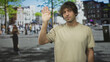 © Krakenimages.com - Young hispanic man raises his right hand with palm facing camera on a busy street plaza with blurred pedestrians; quiet contemplation.