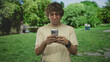 © Krakenimages.com - Man standing and texting on smartphone with hands visible near pond and trees in park; frustration isolation solitude.
