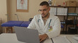 © Krakenimages.com - Man in white coat with stethoscope pointing finger to laptop screen and reviewing patient chart in clinic building; concentration.