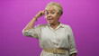 © Krakenimages.com - Senior hispanic woman points finger to temple in studio with magenta backdrop, wearing white linen shirt and beige belt; thoughtful.
