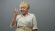 © Krakenimages.com - Woman senior showing peace sign with hand, smiling in beige linen shirt and belt in studio portrait; joyful.