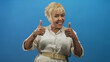 © Krakenimages.com - Senior hispanic woman gives thumbs up and smiles in a blue studio, wearing a belted shirt, bracelets, earrings and rings; joy confidence.