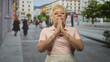 © Krakenimages.com - Woman with hands pressed together in prayer, wearing pink polo and glasses on a pedestrian street with buildings and trees behind; reflection gratitude serenity.