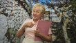 © Krakenimages.com - Senior woman holding a pink clipboard gives thumbs up and points to chest in studio; confidence experience.