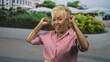© Krakenimages.com - Woman lifts fists by ears and smiles in a sunny street plaza, wearing a red striped shirt and bracelets; joy celebration energy.