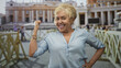 © Krakenimages.com - Woman senior hispanic flexes her fist and smiles while posing in front of a grand building with crowd and railings; confidence and joy.