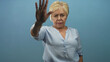 © Krakenimages.com - Woman raises her left hand with palm forward toward camera, eyes closed and focused expression, wearing light blue blouse in studio; determination.