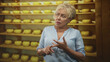 © Krakenimages.com - Woman counting on fingers beside shelves of round cheese wheels in a cheese cellar; thoughtful reflection.