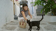 © Krakenimages.com - Woman crouched petting a black cat beside a wicker bag on a white cobblestone street in mykonos, smiling and reaching toward the animal; travel joy.