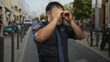 © Krakenimages.com - Young chinese policeman in dark uniform forms hand binoculars to eyes on crowded street; vigilance duty.