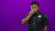 © Krakenimages.com - Man in police uniform with badge visible finger to lips for silence in purple studio with direct gaze; hush order authority discipline.