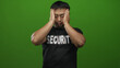 © Krakenimages.com - Young chinese man in security guard shirt holds hands to face with closed eyes in studio against green background; stress.
