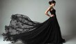 © miss irine - Woman wears long black lace gown with flowing fabric. Strikes confident pose with one hand on hip. Elegant dress intricate floral details, dramatic train flowing behind. Haute couture fashion makes