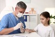 © New Africa - Endocrinologist in medical gloves and protective mask checking little girl's blood sugar level with lancet pen at white desk in clinic