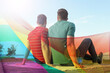 © New Africa - Gay couple sitting near river, double exposure with pride flag