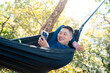 © CandyRetriever  - Move the camera to a quaAsian man relaxing in hammock using smartphone while camping in forest enjoy outdoor active lifestyle leisure travel digital connection social media communicatirter right angle