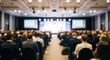 © Hamida - Blurred business conference audience in large hall, defocused corporate seminar crowd, professional convention meeting with stage and screens