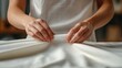 © Larisa AI - Delicate hands are seen smoothing out a pure white fabric, symbolizing craftsmanship, attention to detail, and the tactile aspects of creativity in textile work.