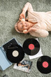 © Pixel-Shot - Mature woman in headphones with record player lying on carpet at home, top view