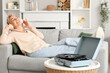 © Pixel-Shot - Mature woman with headphones and record player listening to music on sofa at home