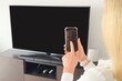 © Angelov - Woman with smartphone connected to TV set in living room