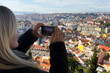 © Angelov - Young woman taking photos with smartphone of Lisbon city, view of the old town Alfama, Portugal, panorama. Lisboa colorful houses and red-tiled roofs.