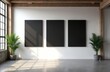 © Maryna - Three blank black canvases hang on a white wall in a minimalist industrial room with large windows. Potted green plants flank the display, adding life to the neutral space.