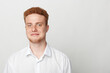 © SHOTPRIME STUDIO - Young man with red hair and beard wearing white shirt smiles gently against plain light background. Portrait of confident male with casual style and natural expression.
