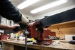 © Stitch - Gloved hands tightening a red metal vise to securely hold a black ski on a workbench