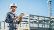© Y Creative Stock - 建設現場でタブレットのデータを確認する作業服姿の日本人現場監督