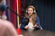 © fizkes - Female host wearing headphones speaking to guest of channel, talking into microphone, recording podcast or digital audio content for vlog in professional studio. Live communication, interview session