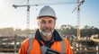 © MDARIF - A construction worker wearing an orange safety jacket and a white hard hat on a building site with cranes